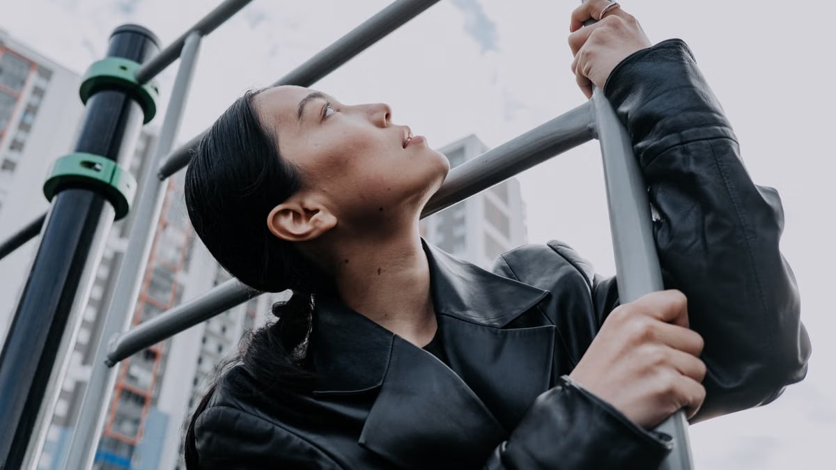 Profile of a woman in a leather jacket posing on a ladder in an urban setting.
